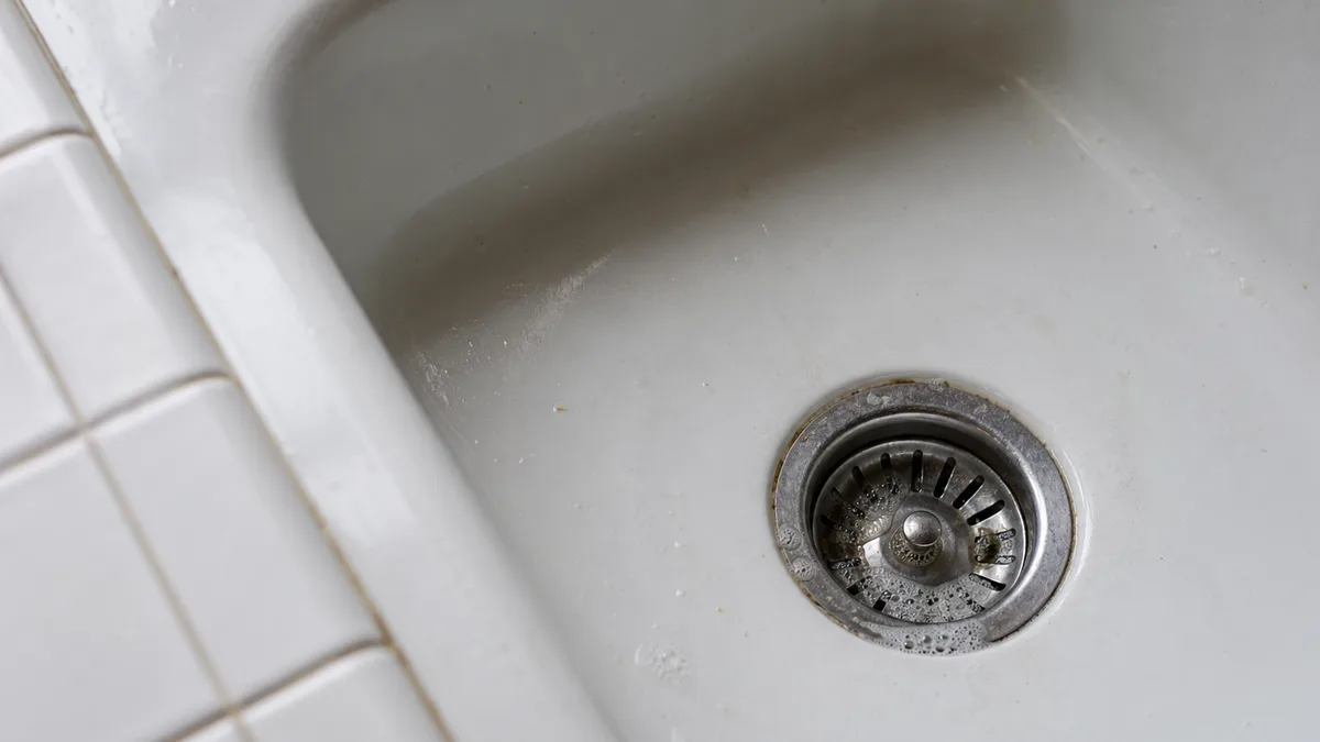 Küchenspüle von oben mit sichtbarem Abflusssieb und Seifenschaum – Reinigung und Pflege des Küchenabflusses