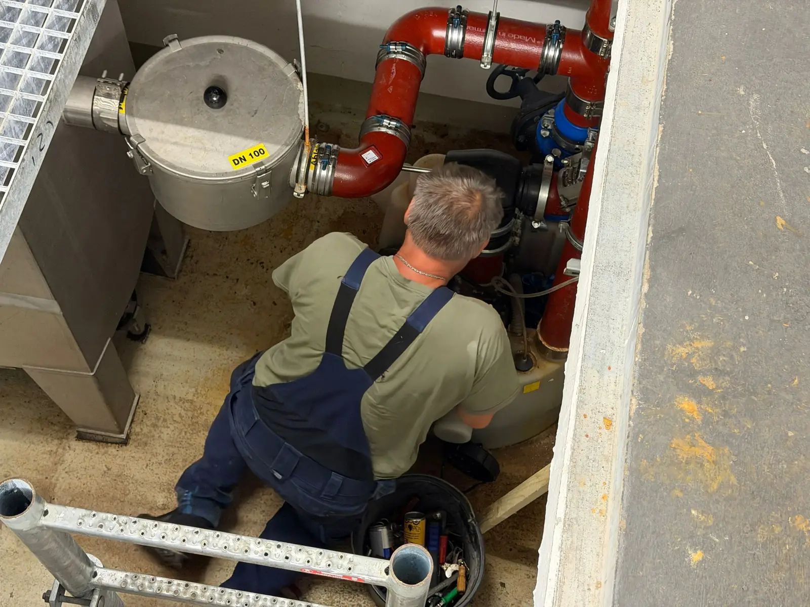 Roland Appel von ABH Rohrreinigung wartet eine Rückstausicherung in einem Pumpwerksschacht mit roten Leitungen